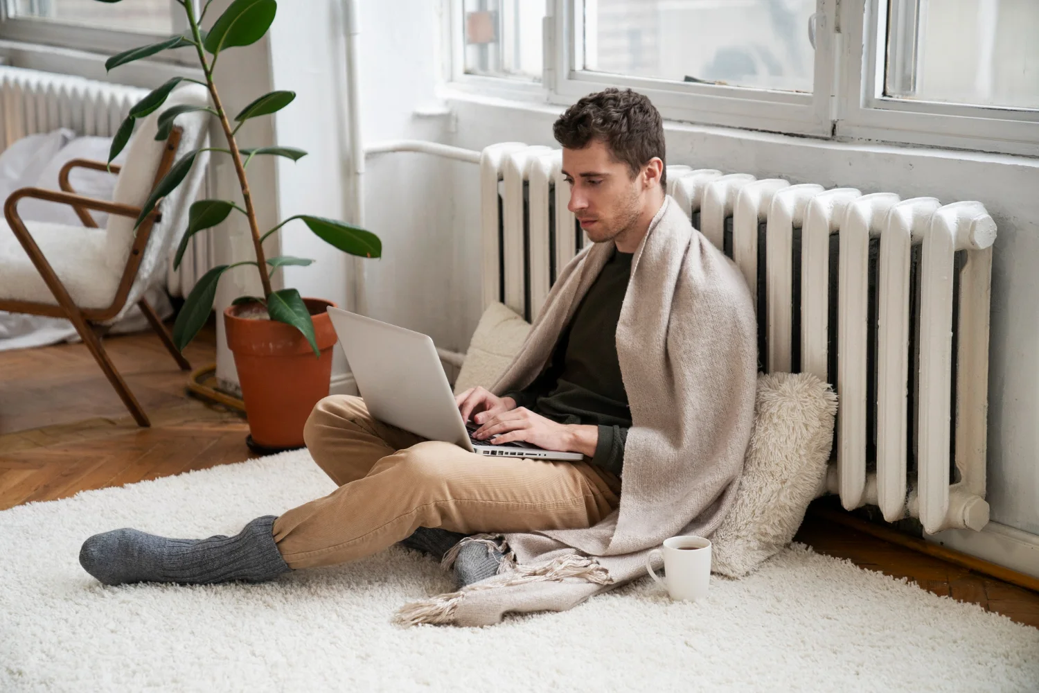 Person relaxing with laptop and coffee in front of their HVAC unit. Featured image for “Find The Right HVAC Settings For Winter In Your Home And Office”.