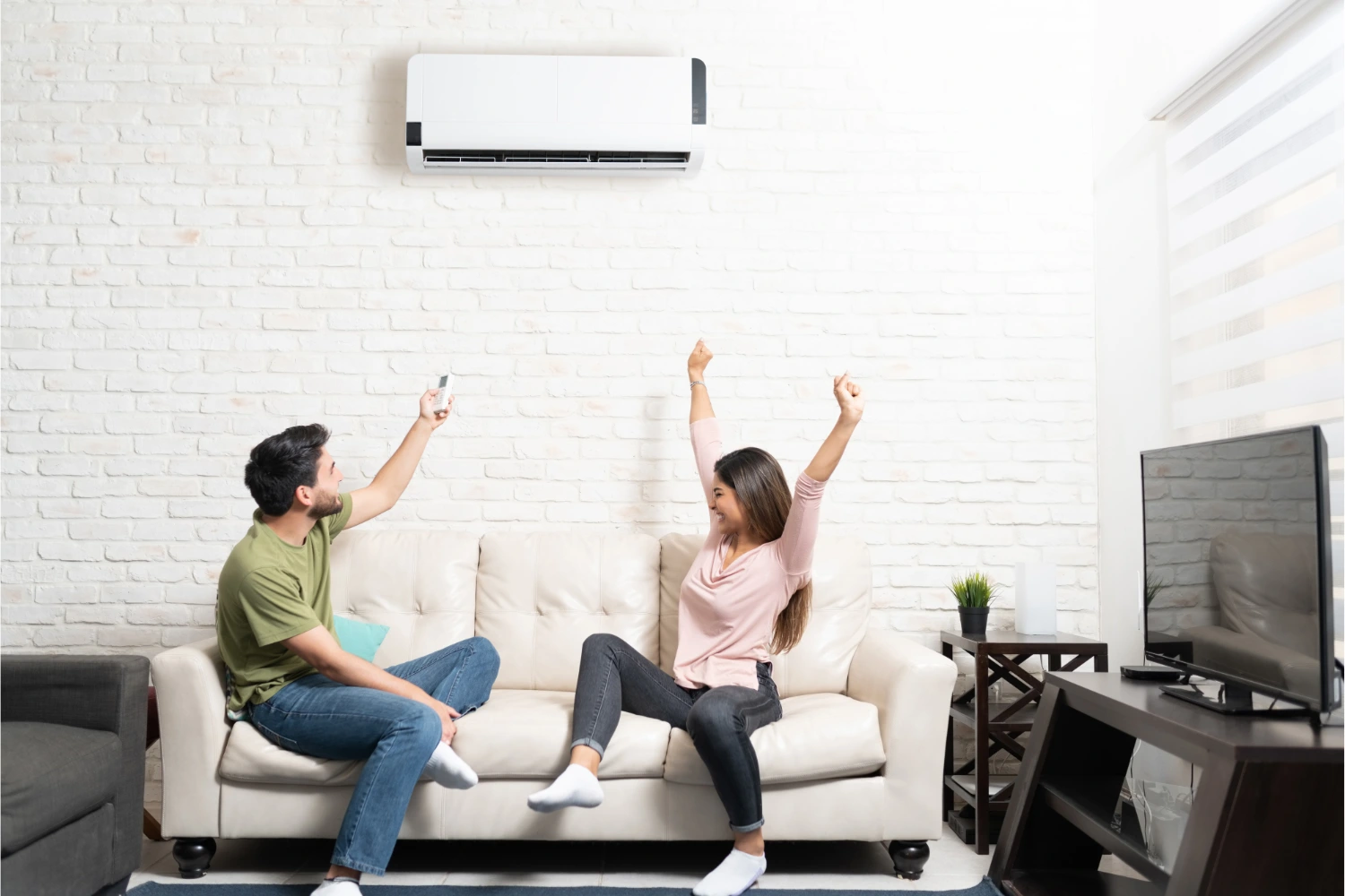 Couple sitting on a sofa below a mini split AC. featured image for “Is a Mini-Split Unit Right for Your Home?”